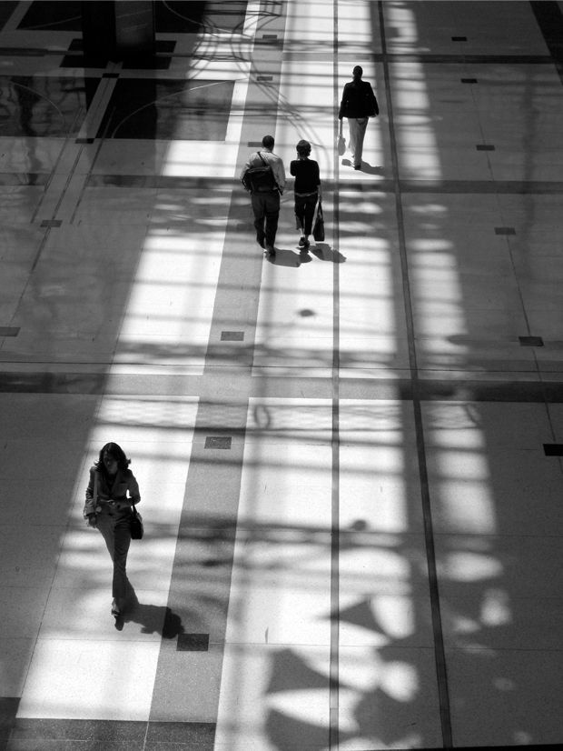 Foto en blanco y negro de varias personas caminando en un andén con fuerte contraluz y contraste