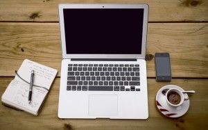 Vista cenital de un portátil, un cuaderno de notas, un móvil y un café sobre una mesa de madera